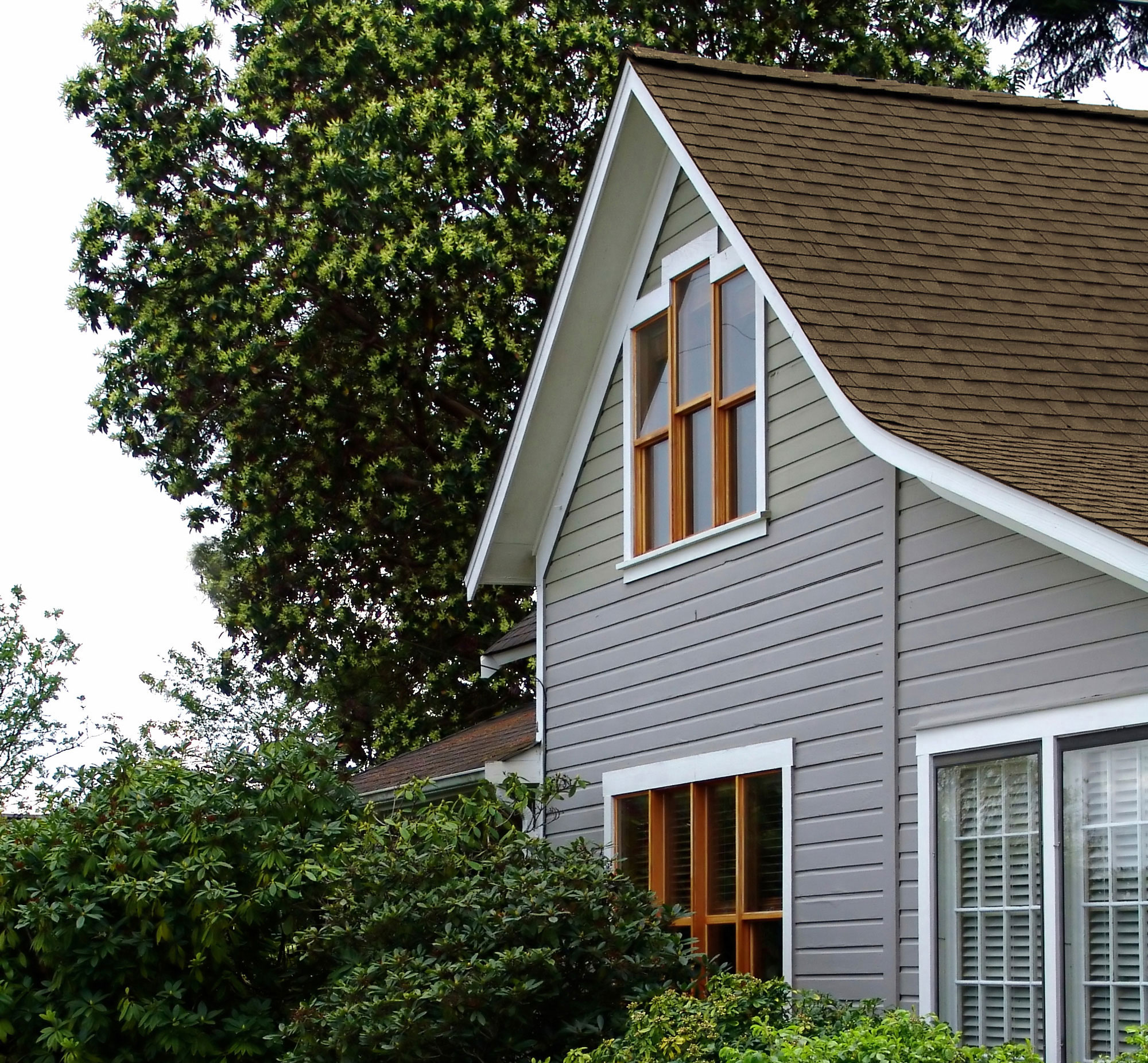 side of gray house with brown shingle roof 